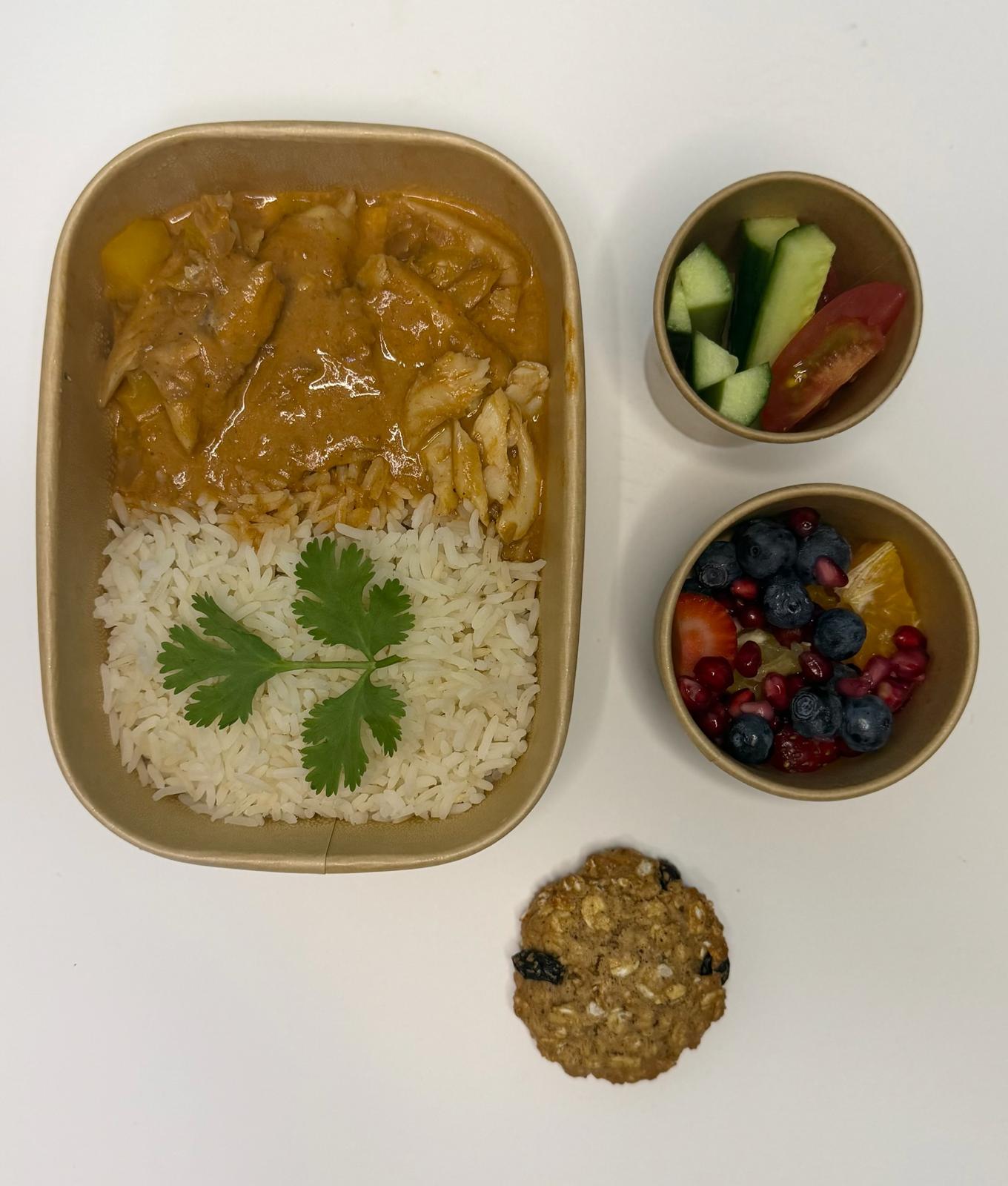 Chicken curry with rice, fresh cucumber and tomato, and a fruit pot